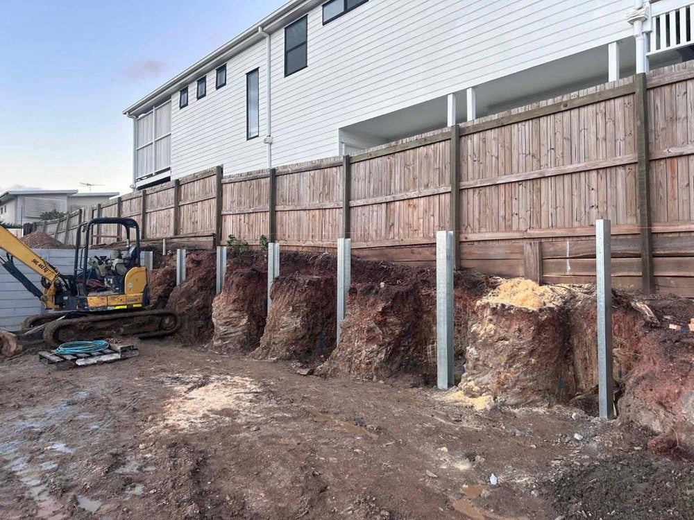 Excavator on a site cut with steel retaining wall posts set into the bank