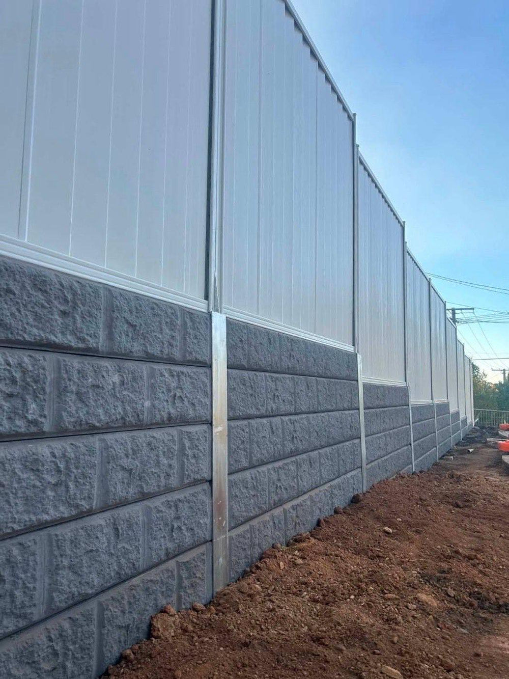 Long concrete block retaining wall with white Colorbond fence on top