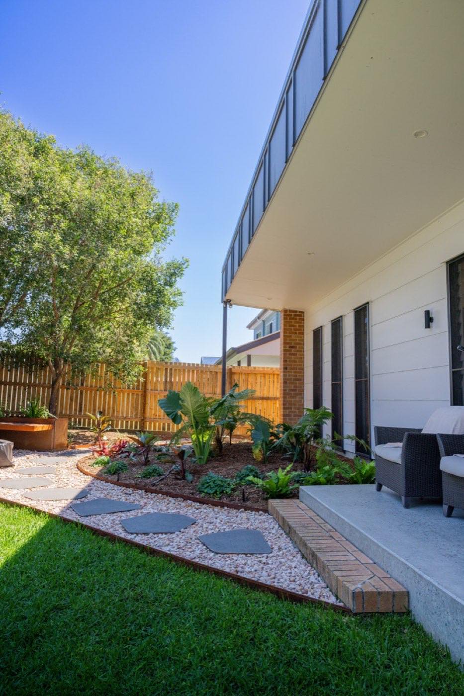 Curved garden bed with stepping stones and turf beside a new home