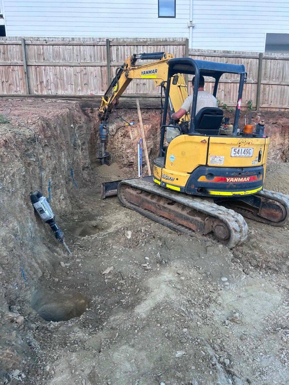 Excavator augering engineered footing holes for a retaining wall