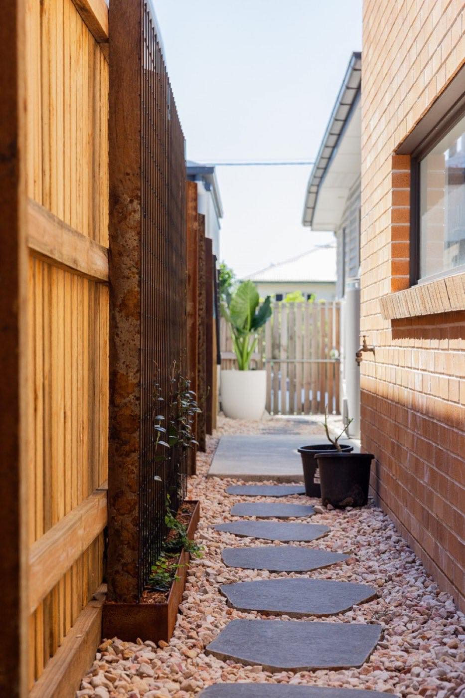 Timber paling fence along a brick side wall with stepping stone path