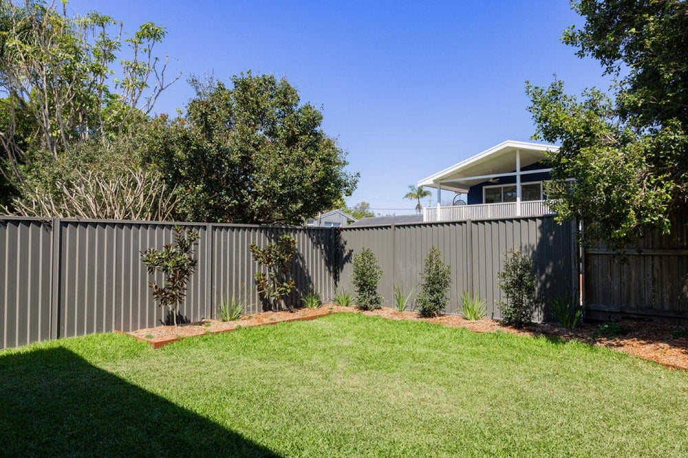 New turf and garden bed along a Colorbond boundary fence