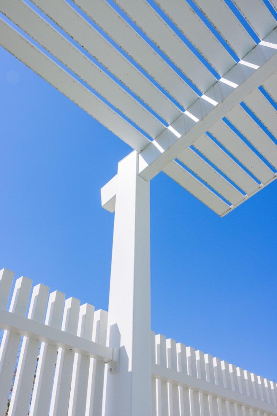 White aluminium slat fence and pergola against a blue sky