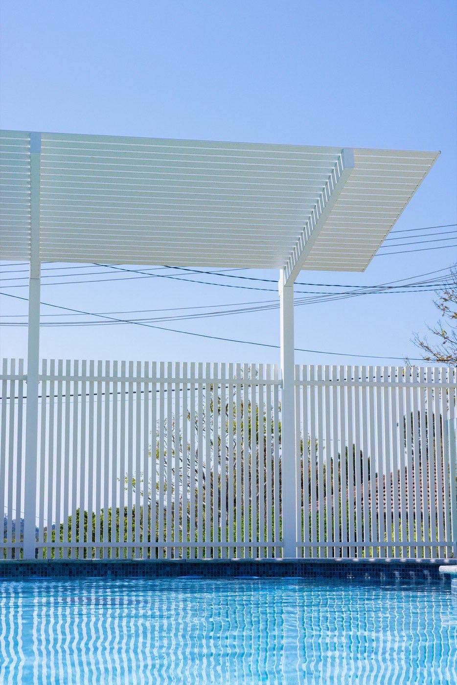 White slat pool fence with pergola beams overhead